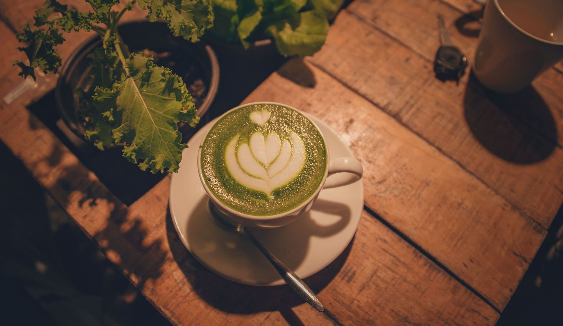 A warm indoor scene of a matcha latte with beautiful latte art on a rustic wooden table.